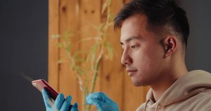 Young asian man send voice audio message recognition with phone wearing protective mask on a phone video call in hospital, standing by a window, coronavirus isolation.