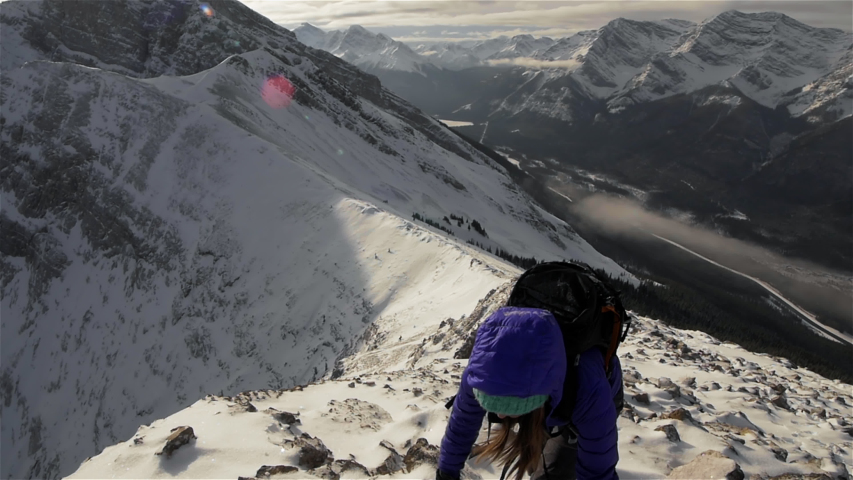 An adventure woman climbing a snowy mountain in Alberta, Canada during sunrise. A female summits Ha Ling Peak in Alberta, Canada during winter. A snowy adventure.   Royalty-Free Stock Footage #1051923232