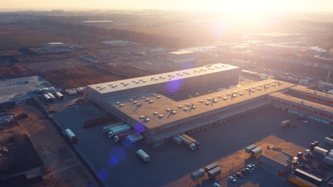 Aerial panoramic view of the big logistics park with warehouse, loading hub with many semi trucks with cargo trailers standing at the ramps for loading/unloading goods