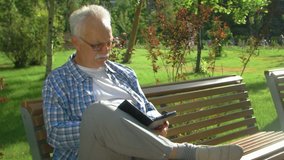 Friendly handsome old man with ebook in park - Powered by Shutterstock - Get 15% off with code: PIKWIZARD15