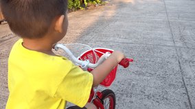 Happy Asian cute cheerful little child boy playful funny enjoy riding a bike red bike bicycle at asphalt road in Housing estate at sunset, Video 4K resolution