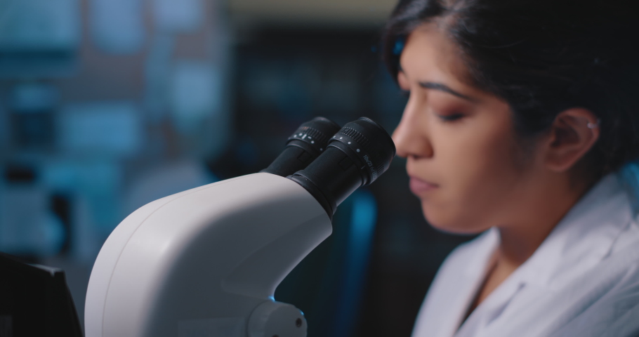 Female research scientist looking at samples under microscope.Blue lighting in a dark lab room.Close up, slider, slow motion, shot with BMPCC 4K.Biochemistry, pharmaceutical medicine, science concept
 | Shutterstock HD Video #1051944406