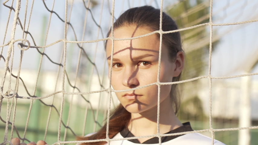 Portrait of young serious woman football player wearing uniform looking into camera in soccer gate at sport field. World Cup Game