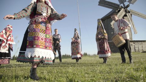 People in traditional russian clothes dancing and singing song outdoor on traditional antique wooden windmill background. Group of happy people wearing national Finno-Ugric clothes.