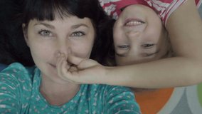 Family selfie. Excited young mother and child playing lying on the floor and taking a selfie. Mother and daughter monkeying around on camera and kissing. Portrait of mom and baby closeup. Slow Motion.