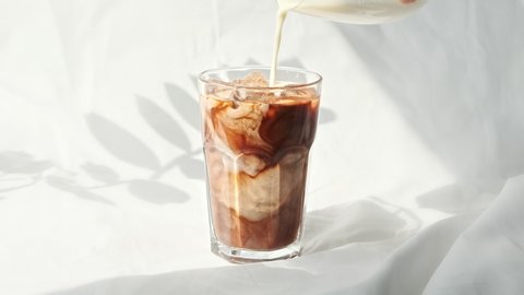 Milk cream is poured into a iced coffee.  Coffee cold drink with ice and milk.