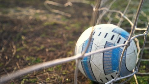 Kyiv, UKRAINE - January 2, 2020: Football goal. The ball flies into the goal. Soccer player scores a goal. Close-up of the grid. Old football field. Street sport. Child Game. The sun shines.