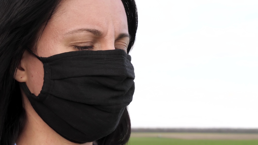 Face of a girl in a black mask close-up. A masked woman inhales the scent of flowers through a protective mask. Concept of protection against virus and seasonal allergies.
