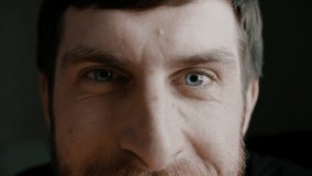 Attractive bearded man partly portrait with blue iris eyes, eyebrows and nose. Young man is looking at the camera and smiles with wrinkles around the eyes. Slow motion portrait close up 4K video.