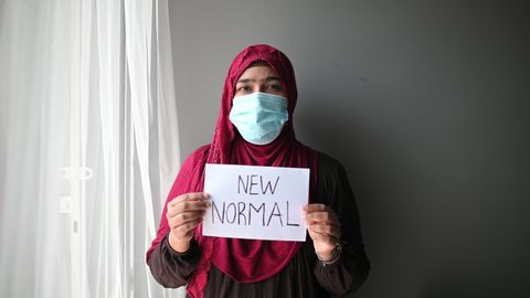 Young beautiful Muslim woman in medical mask, looking at camera and show drawing "NEW NORMAL" to Prevent Disease and Dust, pm.5,Stay at home quarantine coronavirus pandemic prevention.