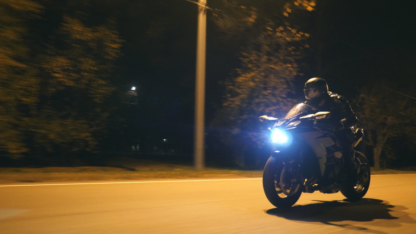 Young man in helmet riding fast on modern black sport motorbike at evening city street. Motorcyclist racing his motorcycle on night empty road. Guy driving bike. Concept of freedom and hobby. Close up Royalty-Free Stock Footage #1051964050