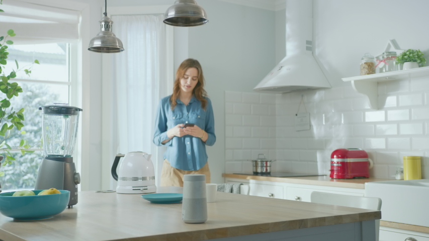 Internet of Things Concept: Beautiful Young Woman Using Smartphone in the Kitchen. She controls her Kitchen Appliances with IOT. Graphics Digitalization Visualization of Connected Home Electronics  | Shutterstock HD Video #1051965454