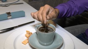 In a restaurant, a man sitting at a table with a spoon stirs coffee with sugar.  Slow motion video Full HD.