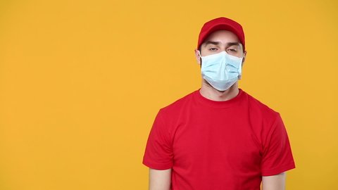 Delivery man in red cap blank t-shirt sterile face mask gloves pointing aside isolated on yellow background studio Guy employee courier Service quarantine pandemic coronavirus virus covid-19 concept
