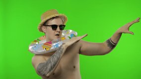 Shirtless young happy man tourist with swimming ring celebrates and dances. Portrait of blonde guy in hat and sunglasses isolated on chroma key background. Place for your logo or text - Powered by Shutterstock - Get 15% off with code: PIKWIZARD15