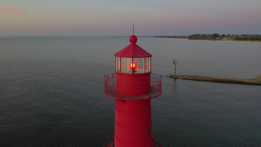 Iconic Lighthouse beacon silhouetted against fiery Lake Michigan twilight horizon, moving aerial view.