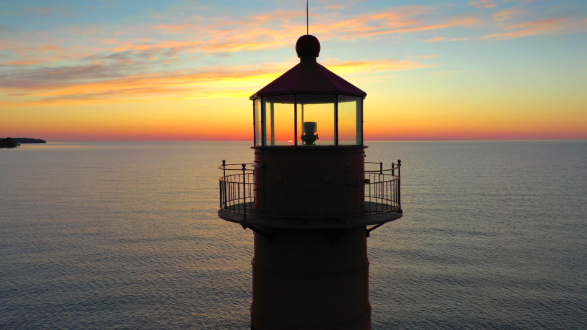 Iconic Lighthouse beacon silhouetted against fiery Lake Michigan twilight horizon, moving aerial view.