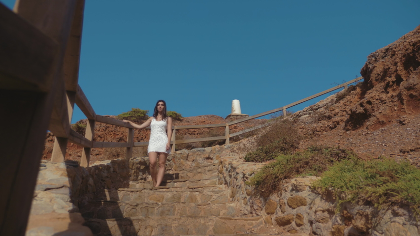 Front shot of a girl going down a cove down the rocky steps of a cliff into the sea.