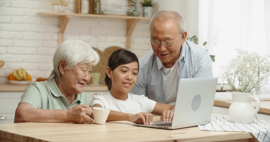 Retired asian couple spending theit time with teen graunddaughter in kitchen, surfing the internet on a laptop - family bonds concept 4k footage | Shutterstock HD Video #1051971241