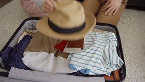 Tilt up closeup of unrecognizable couple packing luggage sitting on floor at home. Man and woman putting clothes, passports and straw hat into suitcase - Powered by Shutterstock - Get 15% off with code: PIKWIZARD15