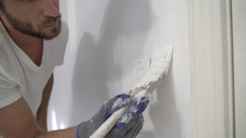 Close up of painter hands with gloves painting the wall edge with brush. A painter edging around light switch with a brush..