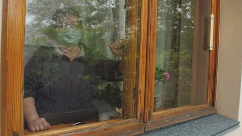 An elderly man in an anti-virus mask with Lily of the valley flowers come to visit his elderly friend, who is in self-isolation. Communication through the window glass.
