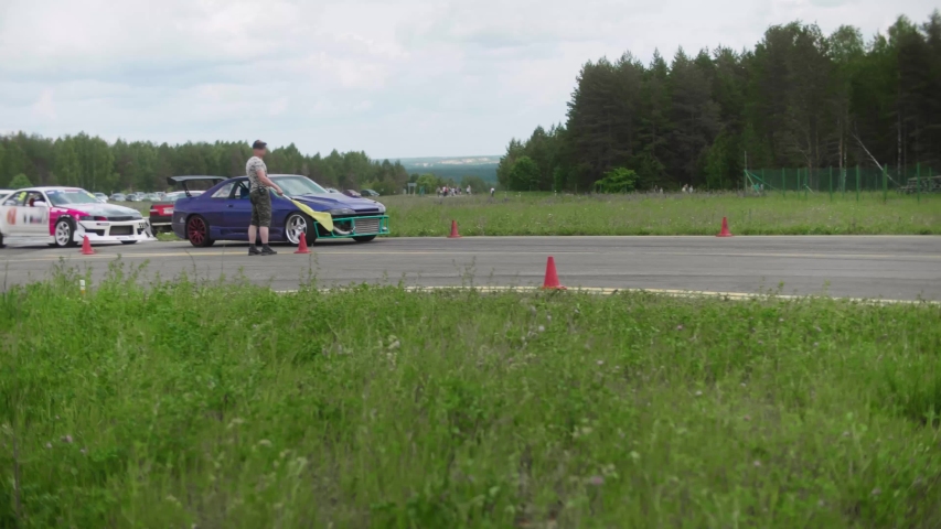 Referee with a yellow flag giving a sign to start, purple car starts riding
