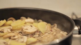 Fried potatoes with mushrooms and onion in a pan with oil using a pan in the restaurant kitchen.