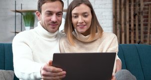 Young Couple surfing in Online Shop while sitting in Loft Living Room. Handsome Male and Female using Laptop on the blue Couch in their own big Flat. Wearing casual Style. Spending Time together.