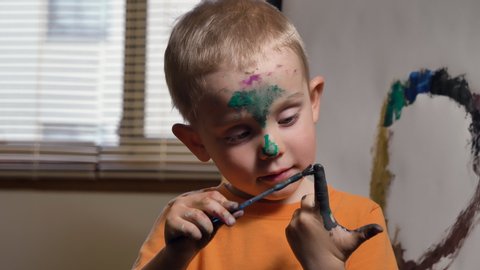 Cute child (Caucasian boy) is having fun, painting his finger.  Kids dirty face and hands after art activities, close up. Fun activity for kids indoor, parenting  concept