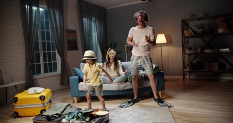 Funny asian family of three happy about upcoming vacation. Mother wearing scuba diver mask meditating while husband and kid are dancing near suitcases - travelling, happy family 4k footage