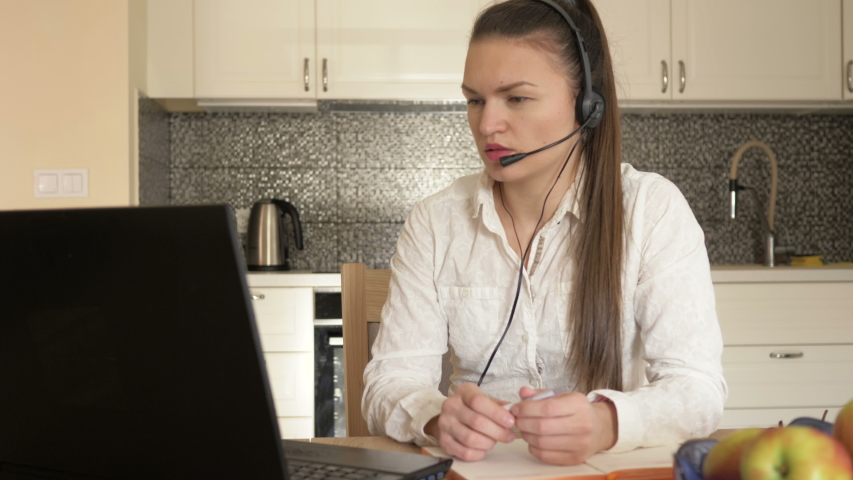 Young woman working at home sits at the kitchen table, looks at the laptop screen and writes something down. Ability to work at home during the coronavirus epidemic.