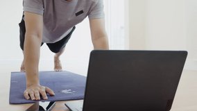 Asian man doing elbow plank up and down exercise in living room at home, watching live or video tutorial online via laptop computer. Activity during quarantine and social distance new normal concept.