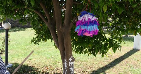 litlle blonde girl hitting pinata to take sweets out under a tree ouside