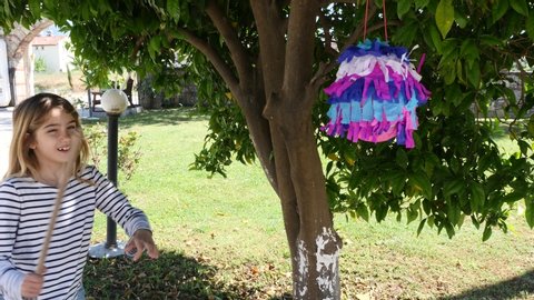 litlle blonde girl hitting pinata to take sweets out under a tree ouside