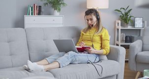 Female student processing a new topic with online tutor, listening through headphones and writing information in notebook. Сoncept of online learning, online courses, remote individual lessons.