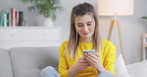 Portrait of happy woman enjoying searching at mobile phone in home office. Surprised lady surfing in Internet at phone in apartment. Joyful girl reading good news on phone in slow motion.