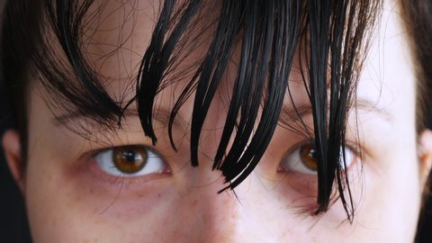 A woman cuts the hair on the head.Herself cut with scissors bangs.Holds hand of the dark strands.Blue comb scratching his hair.Looks up,face closeup shot.A little cuts on the eye,approximately.