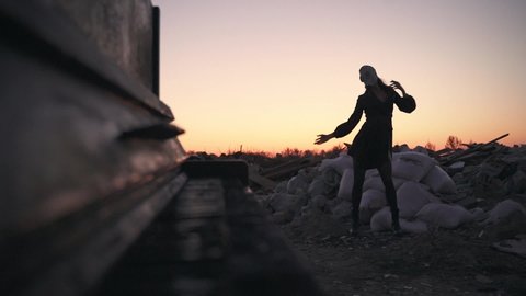 silhouette of a girl in a dress and gas mask dancing in a landfill near the black piano