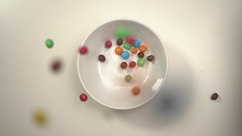Moscow, Russia - 29 04 2020: Color candies M&Ms falling down in white bowl on white table top down view.