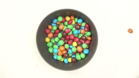 Moscow, Russia - 29 04 2020: Color candies M&Ms falling down in white bowl on white table top down view.