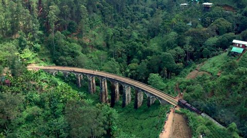 Red train crossing the Nine Arches Bridge in Sri Lanka surrounded by lush green landscape, tea plantations and rolling hills 2