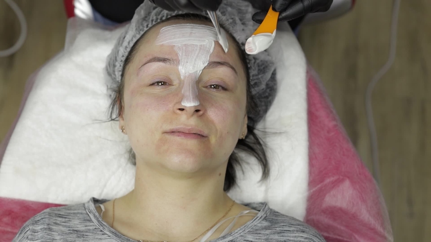 Cosmetologist applying moisturizing cream mask using brush on woman client face in beauty clinic salon. Portrait of female gets medical facial cleaning cosmetology skin acne procedure at spa | Shutterstock HD Video #1052038222