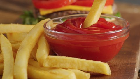 Closeup shot of dipping french fry into ketchup with hamburger in background. Shot on RED 8K camera.