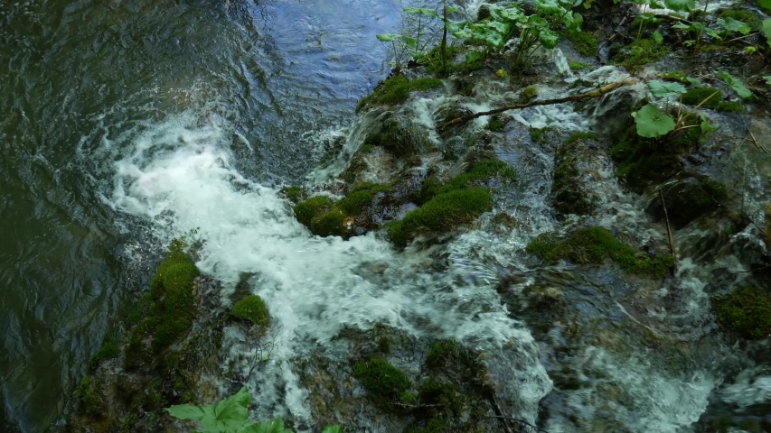 Small waterfalls among the trees on the Plitvice Lakes in the National Park in Croatia. Dense green spring deciduous forest. Top view of the waterfall flowing into the river.