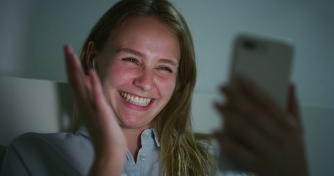 Authentic Shot of an Young Blond Woman is Making a Video Call or Selfie with a Smartphone Before Fall Asleep in a Cosy Bed in a Bedroom at Night. Concept: technology, new generation,family, connection