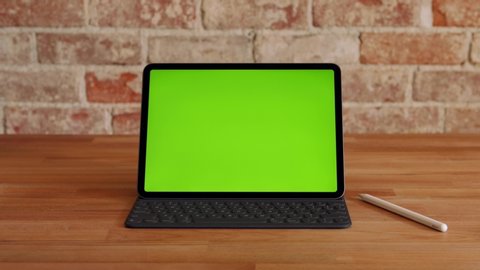 Los Angeles, California / USA - May 7, 2020: Minimal desk setup with an Apple iPad Green Screen and an Apple Pencil on an Apple Magic Keyboard on a wooden desk against a brick wall
