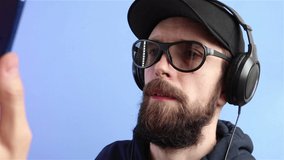 bearded man in cap sunglasses headphones  recording video on smartphone live streaming online translation on blue background