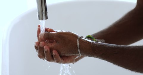 African man washing dirty hands rubbing using sanitizer soap, rinsing under warm running water above bathroom sink. Coronavirus protection hygiene, covid 19 prevention, skincare concept. Close up view