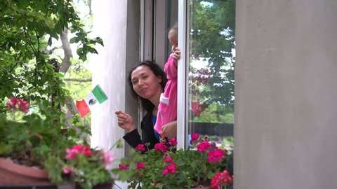 Cinco de Mayo. Independence day. Mexican hispanic family mother and little girl child on balcony window are smiling and waving the flag of Mexico